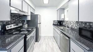 Una cocina moderna con electrodomésticos de acero inoxidable, una encimera negra y un salpicadero de azulejos.