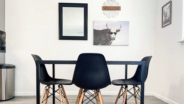 Un comedor moderno con una mesa y sillas negras, un cuadro enmarcado y un cartel con la palabra 'WELCOME' en la pared.