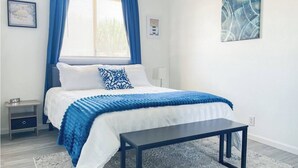 Un dormitorio moderno con una cama, una mesita de noche, un banco y una ventana con cortinas.