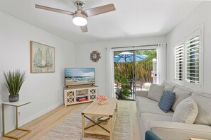 Un salon comprenant un canapé, une table basse, un téléviseur, un ventilateur de plafond et une vue sur l’extérieur, visible à travers la porte vitrée.