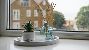 Une petite plante en pot et un flacon en verre contenant des tiges de roseau, le tout posé sur un plateau blanc près d’une fenêtre.