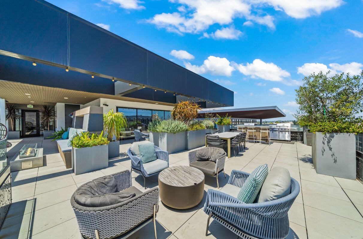 Area patio esterna con mobili moderni, grandi fioriere e vista su un edificio.