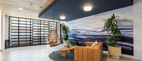 Ein modernes Interieur mit Holzbalkendecke, einer großen Wandmalerei mit Meereslandschaft, einem braunen Sofa und Topfpflanzen.