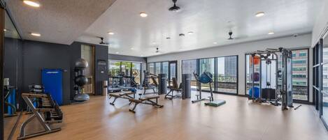Un gimnasio espacioso con diverso equipo de ejercicio, ventanas amplias y un techo alto.