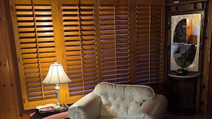 Ein Zimmer mit einem großen Bett, Holzjalousien, einer Lampe und einem Spiegel.