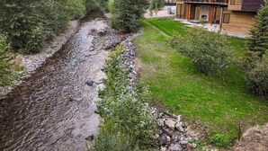 A modern house with a river, surrounded by greenery and mountains.