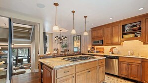 A modern kitchen with wooden cabinets, a central island, stainless steel appliances, pendant lighting, and a view to a balcony.