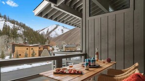 A wooden deck with a table set for a meal, overlooking a snowy mountain landscape.