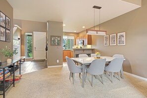 Eine moderne Küche mit Holzausstattung, ein Essbereich mit weißem Tisch und grauen Stühlen sowie ein Teppichboden.