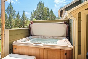 Ein Whirlpool mit Holzverkleidung, vor einer Baumlandschaft und einem Haus gelegen.