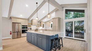 Une cuisine moderne dotée d’un grand îlot central, d’appareils électroménagers en acier inoxydable et de luminaires suspendus.