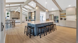 Une cuisine spacieuse dotée d’un îlot central, de tabourets de bar, de luminaires suspendus et d’un mur en briques en arrière-plan.