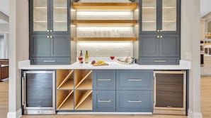 Une cuisine moderne avec des meubles de couleur sombre, un réfrigérateur à vin encastré et un îlot central doté d’un plan de travail clair.