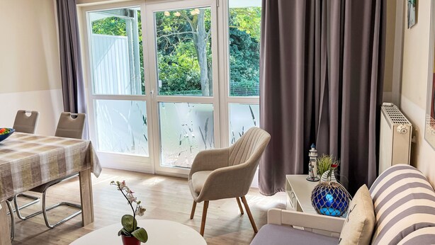 Habitació moderna amb taula de menjador, un sofà, una cadira i una finestra gran amb cortines.
