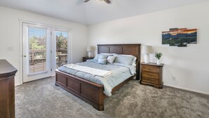 A bedroom with a bed, a nightstand, a ceiling fan, a door with blinds, and a wall-mounted painting.