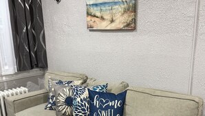 A beige sectional sofa with decorative pillows, a wall-mounted picture, and a radiator. - AC’s Finest! (Atlantic City)