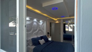 Ein Schlafzimmer mit großem Fenster, einem Bett mit blauer Bettwäsche und einem modernen Kopfteil.