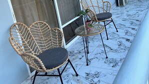 Ein Balkon mit zwei Korbstühlen, einem kleinen Tisch, einer Schiebetür und einer Wand-Klimaanlage.