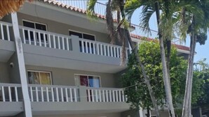 Ein mehrstöckiges Hotel mit Balkonen, einem Schwimmbad und Palmen.