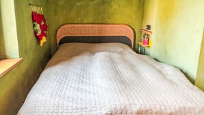 A single bed with a patterned bedspread, a woven headboard, and a wall-mounted shelf with a small decorative item.