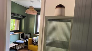 A room with a yellow chair, a desk, a window with blinds, and a hanging light fixture.