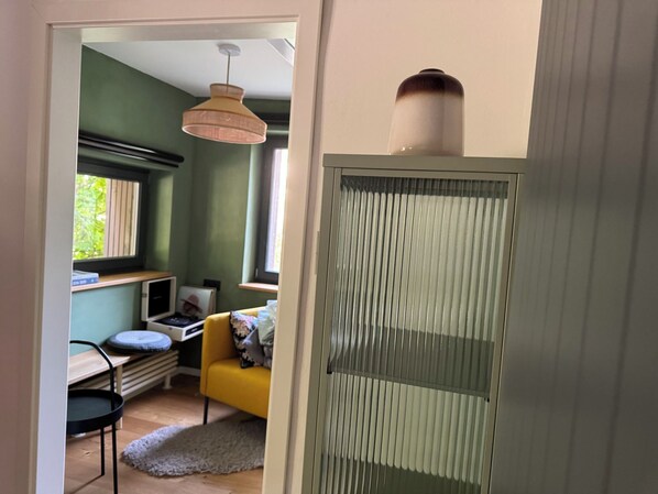 Una habitación con una silla amarilla, un escritorio, una ventana con persianas y una lámpara colgante.
