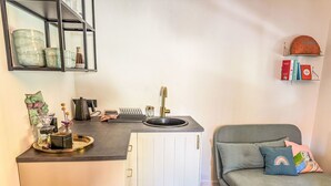 A compact kitchen with a sink, white cabinets, and a grey sofa with colorful cushions.