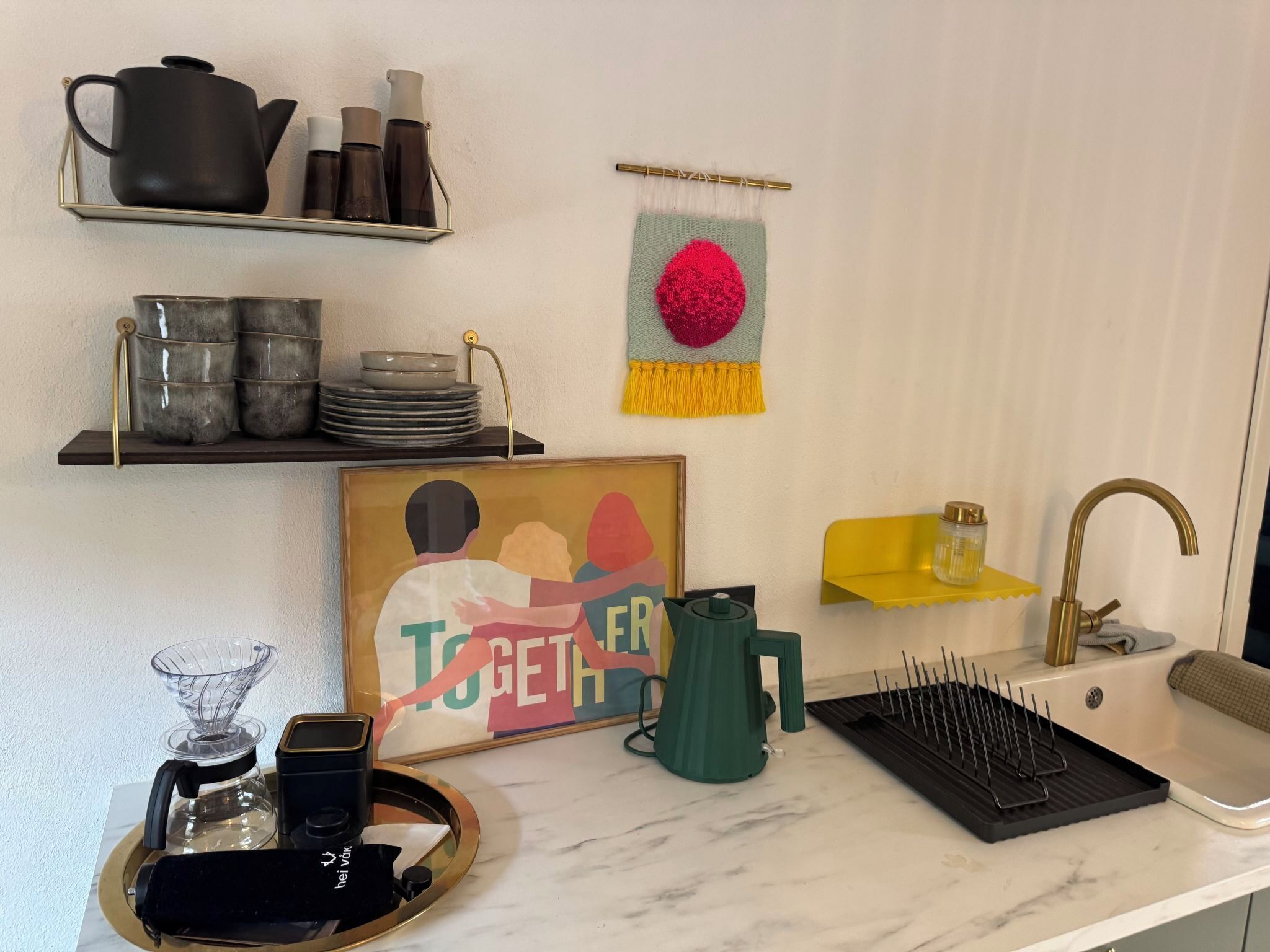 A kitchen with a marble countertop, a coffee maker, a kettle, a sink, and a framed picture with the word "TOGETHER".