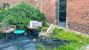 A brick building with a glass door and a small garden area with wicker chairs and a round table. - Hinterhov Koje by Interhome (Beeskow)