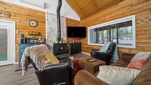 A cozy cabin-style room with a fireplace, wooden walls, a television, and a comfortable seating area.