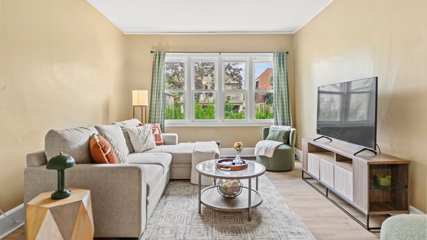 A living room with a sofa, coffee table, TV stand, and a window with curtains. - Brady St Retreat Front House - Sleeps 8 & Pets (Milwaukee)