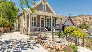 A two-story house with a porch, a stone wall, and a mountain in the background. - Historic Gem in Virginia City (Virginia City)