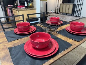 A dining table with red plates and bowls, black placemats, and a black chair in the background.
