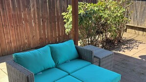 A wicker outdoor sofa with teal cushions, set on a concrete patio with a wooden fence and greenery in the background. - Charming 2-bedroom townhome - All brand new - pets welcome (Sacramento)