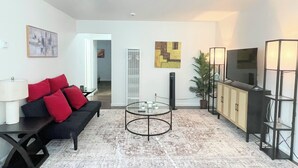 A modern living room with a black sofa, red cushions, a glass coffee table, a flat-screen TV, and a potted plant. - Charming 2-bedroom townhome - All brand new - pets welcome (Sacramento)