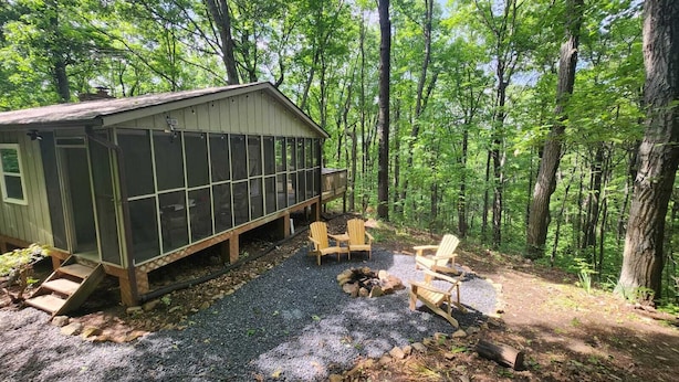 A cabin with a covered porch, outdoor seating, and a fire pit in a forested area. - Charming 2-bedroom cabin in delightful New Market with AC (New Market)