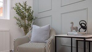Un sillón a rayas con un cojín claro, una mesita con libros y un objeto decorativo, y una planta en maceta.