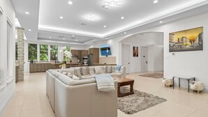 Un vaste espace de vie comprenant un grand canapé beige, une table basse et une cuisine en arrière-plan.
