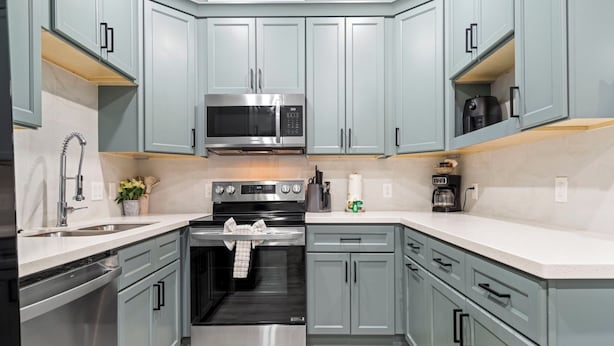 Cocina moderna con armarios grises, electrodomésticos de acero inoxidable y encimera blanca.