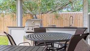 Un patio al aire libre con una parrilla, una mesa redonda y sillas.