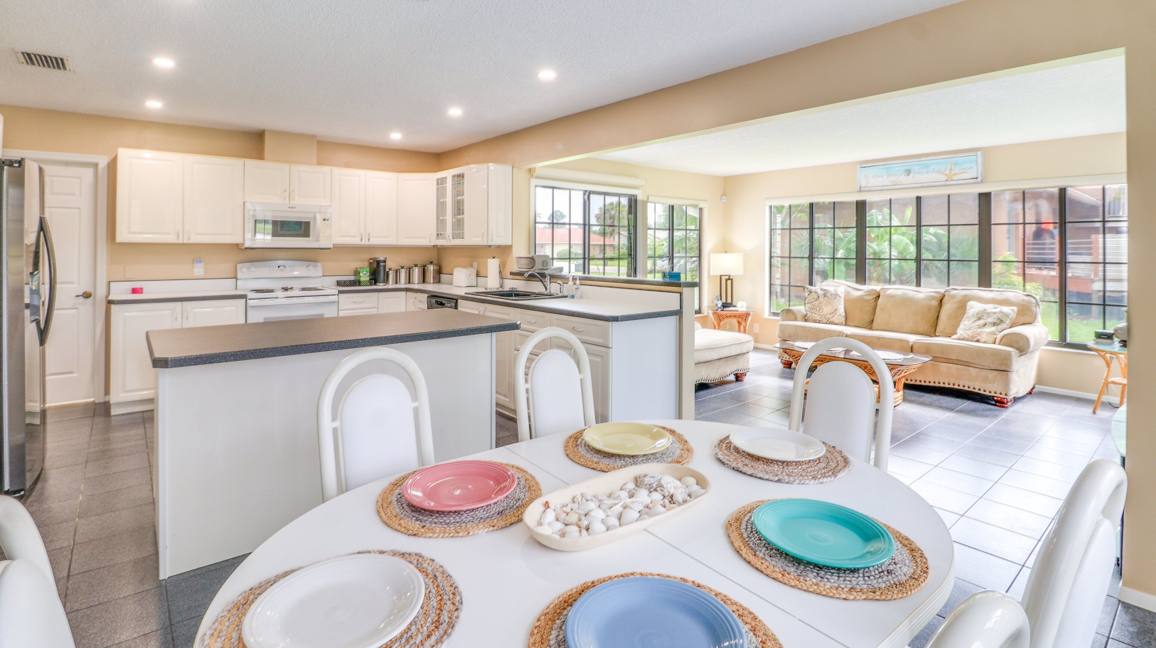 Een moderne keuken met witte kastjes, een centraal eiland en een eetgedeelte met een ronde tafel voor vier personen.