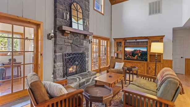Una sala de estar acogedora con chimenea de piedra, muebles de madera y un amplio ventanal con vistas a una terraza.