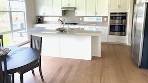 A modern kitchen with white cabinets, a stainless steel refrigerator, and an island with a sink. - Delaware getaway near Bethany Beach (Ocean View)