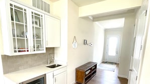 A kitchen with white cabinets, a stainless steel sink, and a built-in oven. There is a wooden bench with a towel draped over it. The floor is wooden, and the walls are painted white. - Delaware getaway near Bethany Beach (Ocean View)