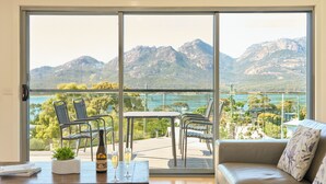 A balcony with a table, chairs, and a sofa overlooking a mountainous landscape. - Deja Blue 1 - Freycinet (Glamorgan-Spring Bay)