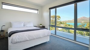A bedroom with a large bed, a bedside table, a nightstand, a window with a view of a landscape, and a ceiling light. - Deja Blue 1 - Freycinet (Glamorgan-Spring Bay)