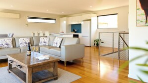 A modern living room with a sofa, coffee table, and a kitchen area in the background. - Deja Blue 1 - Freycinet (Glamorgan-Spring Bay)