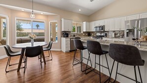 A modern kitchen with white cabinets, a granite countertop, and a dining area with a table and chairs. - Sun and Shade Oasis  by J and Amy BL 991449 (Mesquite)