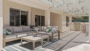 A covered outdoor patio with a sofa, coffee table, and grill area. - Sun and Shade Oasis  by J and Amy BL 991449 (Mesquite)