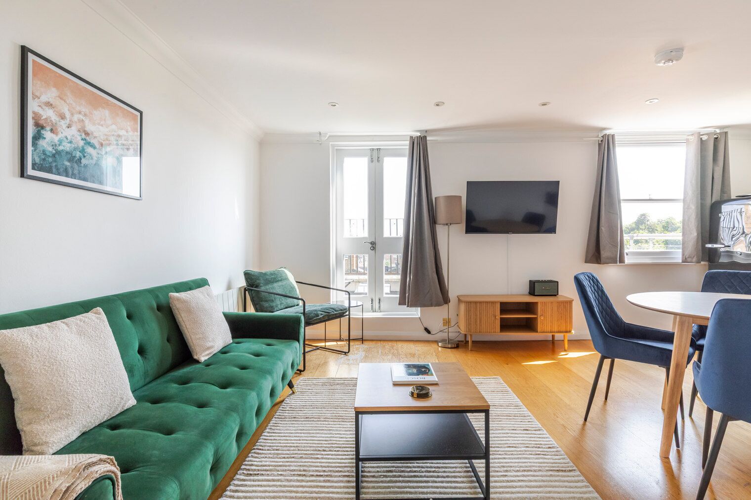 Un salon moderne avec un canapé vert, une table basse, un téléviseur et un coin repas comprenant des chaises et une table.